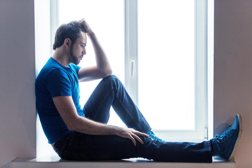 sad young man sitting on the floor wearing jeans and blue shirt