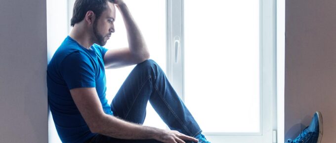 sad young man sitting on the floor wearing jeans and blue shirt